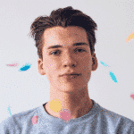 A young person with short hair, wearing a gray sweater, stands against a plain background. In an air of Incogniton, colorful confetti pieces float around them, adding an element of surprise and delight.